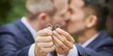 Two men holding wedding rings whilst kissing